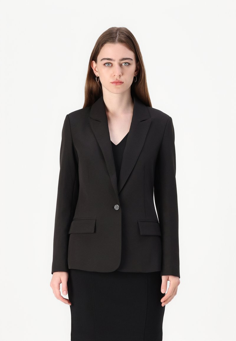 Svart skreddersydd blazer med reverskrage, to frontlommer og enkle knappekrage. Glatt stoff med strukturert passform.