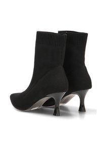 Botas de calcetín negras de punto con punta afilada y tacones curvados de altura media, mostradas desde atrás y de lado.