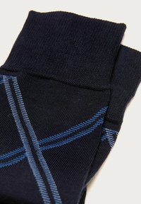 Calzini blu scuro con un motivo geometrico in blu chiaro, realizzati in morbido tessuto a maglia, con un design a costine sulla parte superiore.