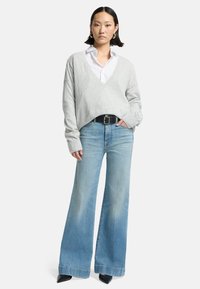 Light gray oversized sweater with a V-neck, paired with wide-leg light blue jeans. Black belt and pointed black heels complete the outfit.