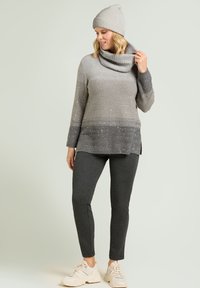 Suéter con degradado gris y cuello de tortuga, con destellos metálicos, combinado con pantalones gris oscuro y zapatillas crema, completado con un gorro gris a juego.
