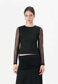 Black long-sleeve top with sheer mesh sleeves, round neckline, and fitted design. Paired with a black ruched skirt. Smooth texture.