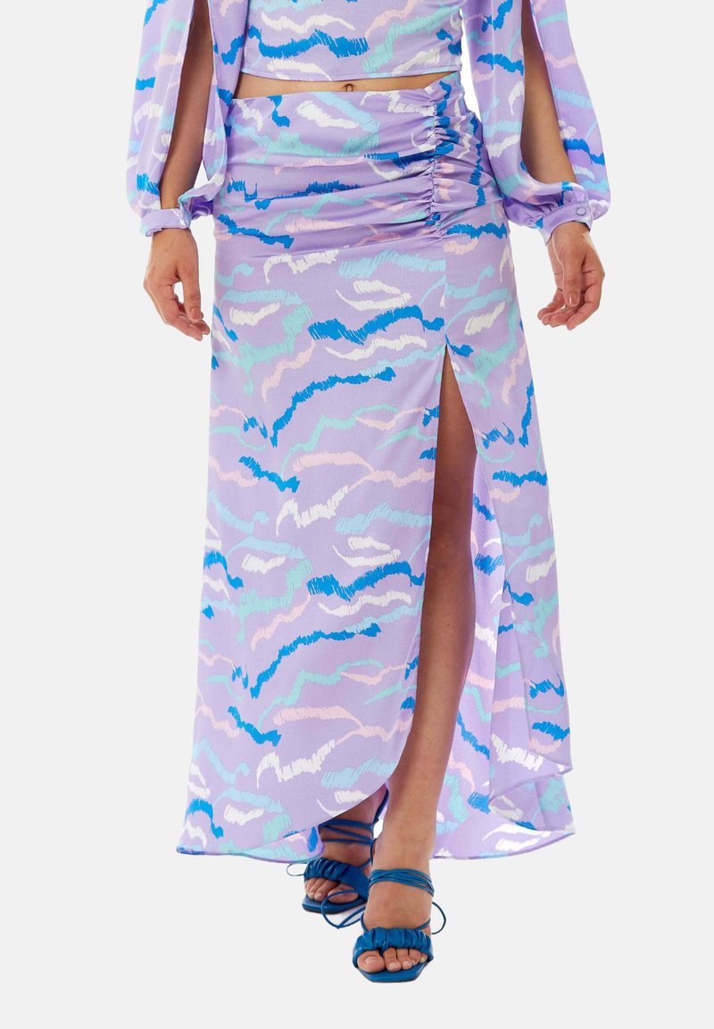 Lavender, patterned midi skirt with ruching on the side, featuring a high slit and textured fabric. Paired with blue strappy sandals.