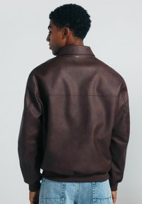 Braune Lederjacke mit lässiger Passform, gerippten Bündchen und Kragen. Sie hat eine glatte Textur und dezente Nahtdetails auf dem Rücken.