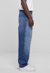 Blå denimjeans med rak passform, med en bakficka och subtila blekningar. Kombineras med vita sneakers för en avslappnad look.