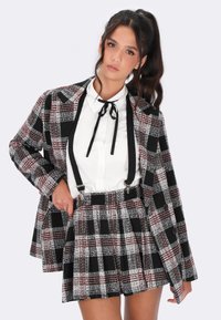 Completo blazer e pantaloni corti in tonalità black, white e red. Il blazer presenta un colletto a ribotino; i pantaloni corti hanno bretelle e pieghe.