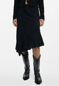 Black flounced skirt with textured fabric and wavy hem, paired with black cowboy boots featuring white embroidered accents.
