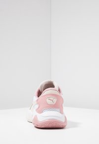 Sportowe sneakersy z białą siateczką i skórzanym wierzchem, różowymi akcentami, teksturowanym kołnierzem oraz gumową podeszwą z falistym wzorem.
