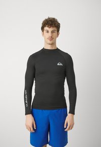 Svart langermet rash guard med rund hals og Quiksilver-logo på brystet og armen, parret med blå shorts.