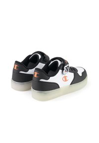 Baskets noir et blanc avec une tige en cuir lisse, des accents orange et une semelle en caoutchouc transparent. Comprend une sangle et un détail de logo au niveau du talon.