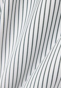 Belo blago s tankimi navpičnimi črnimi črtami in vidnimi gubami, ki ustvarjajo rahlo zguban videz.