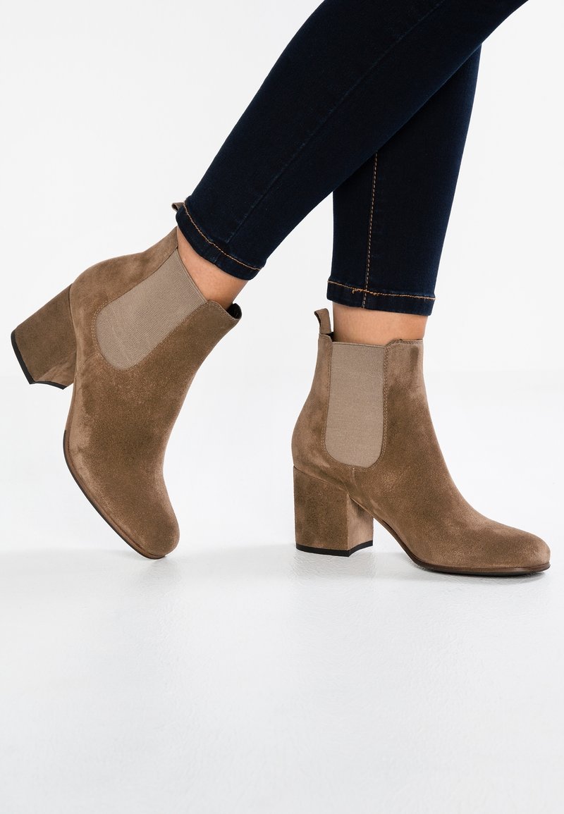 Bottines en daim marron avec talons carrés portées avec un jean skinny bleu foncé sur fond blanc.