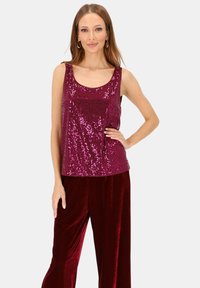 Błyszczący bordowy top na ramiączkach z wykończeniem z cekinów, z okrągłym dekoltem i szerokimi ramiączkami, zestawiony z miękkimi, głęboko czerwonymi welwetowymi spodniami.
