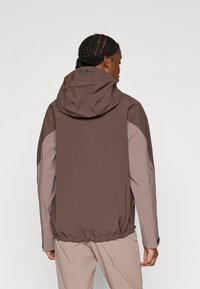 Καφέ και ανοιχτό γκρι μπουφάν με κουκούλα και σφιγμένο τελείωμα, κατασκευασμένο από υφή ύφασμα, με λογότυπο κοντά στον γιακά.