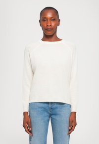 Hvit strikkegenser med rund hals, ribbestrikkede ermer og kant. Kombinert med lyseblå denimjeans. Myk tekstur og avslappet passform.