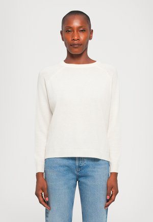 Hvit strikkegenser med rund hals, ribbestrikkede ermer og kant. Kombinert med lyseblå denimjeans. Myk tekstur og avslappet passform.