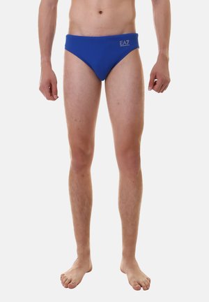 Bañador azul hecho de material elástico, con una cintura plana y un pequeño logo de EA7 en la parte delantera. Textura suave con cobertura mínima.