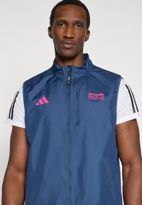 Navy blue lightweight vest with a high collar, front zipper, and pink "BMW Berlin Marathon" logo. Features black striped accents on sleeves.