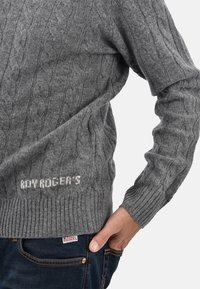 Maglione grigio a maglia grossa con polsini e orlo a coste. Logo "ROY ROGER'S" visibile in basso. Indossato sopra jeans blu.
