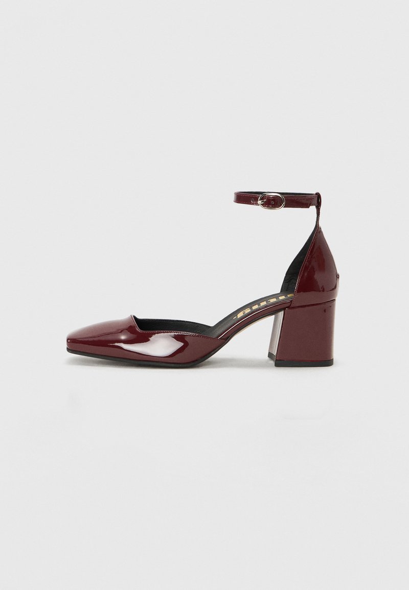 Burgundy patent leather high heel shoe with a pointed toe, ankle strap, and chunky heel. Smooth texture and black interior lining.