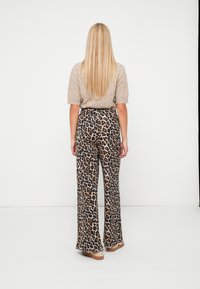 Bež kudumiga lühikeste varrukatega topp, mis on kombineeritud laia säärega leopardimustriliste pükstega. Pükstel on pruunide ja mustade mustrite kombinatsioon. Näha on madalaid jalanõusid.