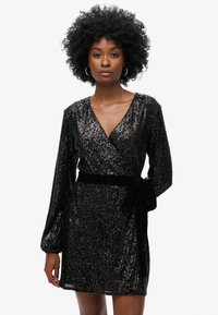 Robe noire à sequins avec manches longues et design wrap, dotée d'une ceinture en velours mettant en valeur la taille. Texture lisse avec des sequins réfléchissants.