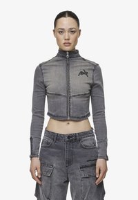 Cropped grey denim jacket with long sleeves, high collar, front zipper, and embroidered logo on left chest. Textured fabric with visible seams.