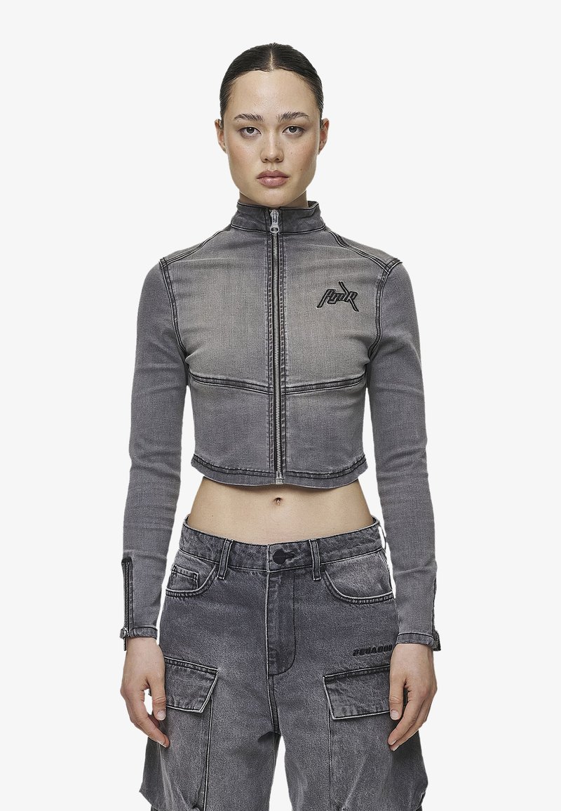 Cropped grey denim jacket with long sleeves, high collar, front zipper, and embroidered logo on left chest. Textured fabric with visible seams.