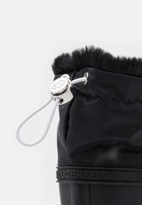 Black waterproof boot with textured fabric upper, fuzzy collar, and elastic drawstring. Features a branded rubber sole for grip.