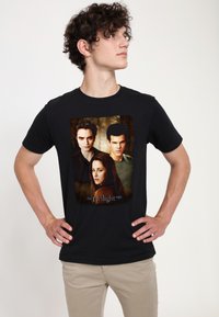 Camiseta de algodón negra que presenta una imagen impresa de tres personajes de "La Saga Crepúsculo". Ajustada, con mangas cortas y cuello redondo.