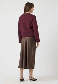 Suéter de punto burdeos con cuello redondo, dobladillo acanalado y mangas largas, combinado con una falda midi de satén marrón suave y zapatos de tacón negros.