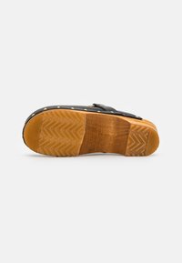 Zwarte leren sandaal met gouden studs, houten tussenzool en een gestructureerde rubberen zool met een visgraatpatroon.
