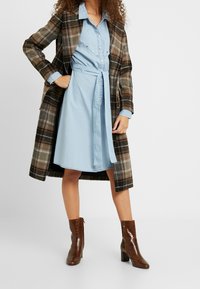 Plaid overcoat in brown, black, and orange; light blue shirt dress with buttons; brown croc-embossed ankle boots.