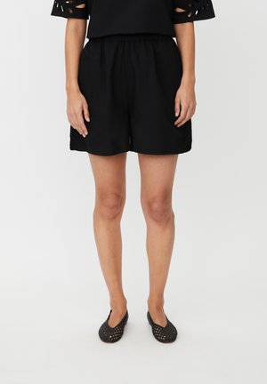 Zwarte, lichtgewicht korte broek met een elastische tailleband, voorzien van een losse pasvorm en subtiel patroon aan de zijkant. Gecombineerd met zwarte mesh instapschoenen.