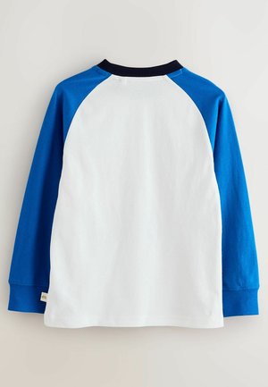 Maglietta a maniche lunghe con corpo bianco e maniche raglan blu. Tessuto in cotone morbido con colletto tondo blu navy e un piccolo tag all'orlo.