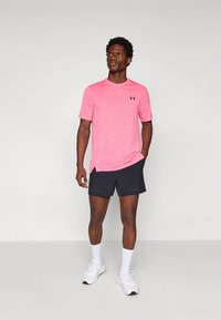 Lyserosa sportst-skjorte med korte ermer, kombinert med mørke shorts, hvite ankelsokker og hvite sportssko. Enkel design og passform.