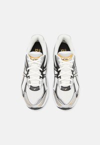 Vita atletiska skor med svarta och guldiga detaljer, övre del i mesh och syntetmaterial, rund tå, vadderat krage och snörning för säker passform.