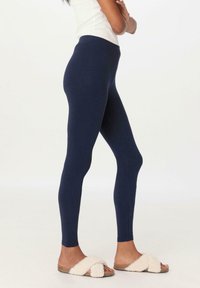 Marineblauwe legging met een gladde, rekbare textuur en een hoge tailleband. In combinatie met tan sandalen met een pluizig strapontwerp.