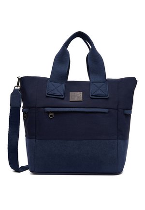 Granatowa torba typu tote z przednią kieszenią na zamek, podwójnymi uchwytami, odpinanym paskiem na ramię oraz prostokątną metką marki na górze z przodu.