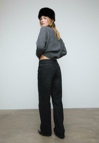 Szary skrócony sweter z prążkowanym dołem; czarne spodnie o wysokim stanie i szerokich nogawkach z kieszeniami i kontrastowym szwem; model nosi czapkę z czarnego futra.