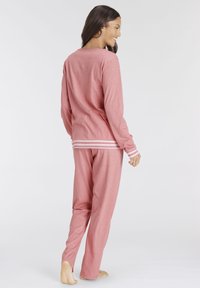 Helles rosa Loungewear-Set, bestehend aus einem Langarmshirt mit weißen Streifen an den Bündchen und passenden Hosen mit lockerem Schnitt und weicher Textur.