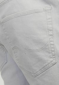 Vaqueros de mezclilla gris claro con un único bolsillo trasero, que presenta detalles sutiles de costura y una textura suave.