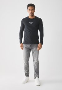 Black long-sleeve t-shirt with "Brooklyn NY" text, paired with faded grey jeans and white sneakers, set against a plain background.