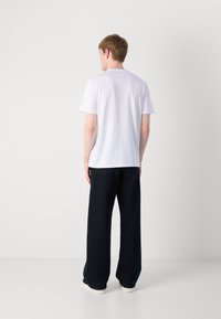 Hvit bomull T-skjorte med kort erm og rund hals, parret med løstsittende mørkeblå bukser. Enkelt design, ingen synlige mønstre.