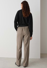 Schwarzer Pullover mit langen Ärmeln und Bündchen, kombiniert mit beigefarbenen, karierten, weit geschnittenen Hosen. Flache Schuhe runden das Outfit ab.