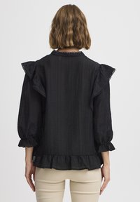 Blusa nera con maniche a sbuffo e dettagli arricciati, in un tessuto strutturato e con un orlo rifinito da un dettaglio arricciato.