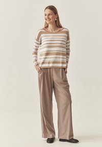 Beež ja valgetriibuline pika varrukaga pluus, millele on sobitatud laiad taupe'i värvi püksid, millel on mugav lõige ja soonikkoes varrukad.