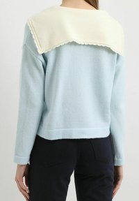 Suéter azul claro con un color blanco ondulado, dobladillo acanalado y mangas largas; textura suave con un diseño ajustado.