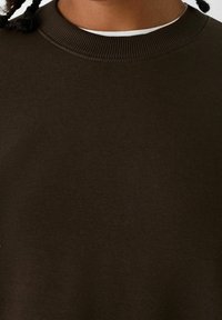 Mörkgrön sweatshirt med ribbad rund hals och slät textur. Tyget verkar mjukt och lätt, perfekt för avslappnad användning.