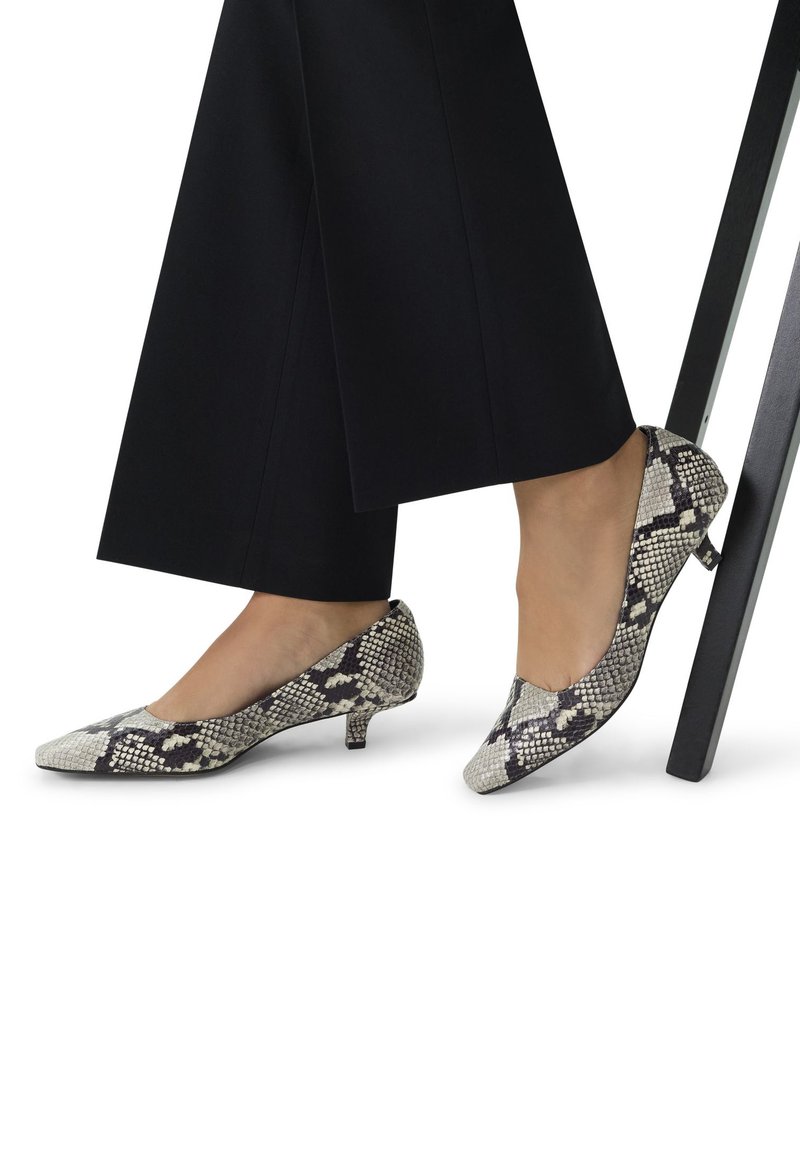Des escarpins à bout pointu en imprimé serpent noir et blanc, avec une texture lisse et des talons bas, associés à un pantalon large noir.